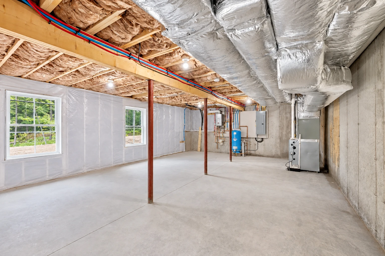 An unfinished basement with fiberglass insulation between ceiling joists, insulated ductwork, windows, and a concrete floor.