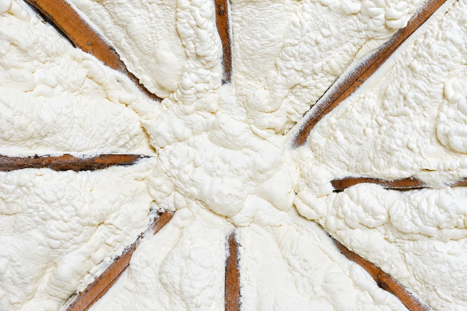 Close-up of thick white closed-cell spray foam filling roof rafters, with brown wooden beams visible through it.